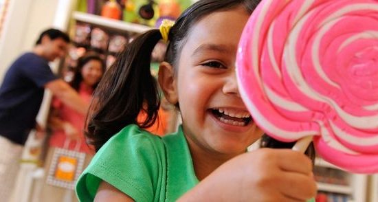 Little girl smiles while holding pink and white lollipop