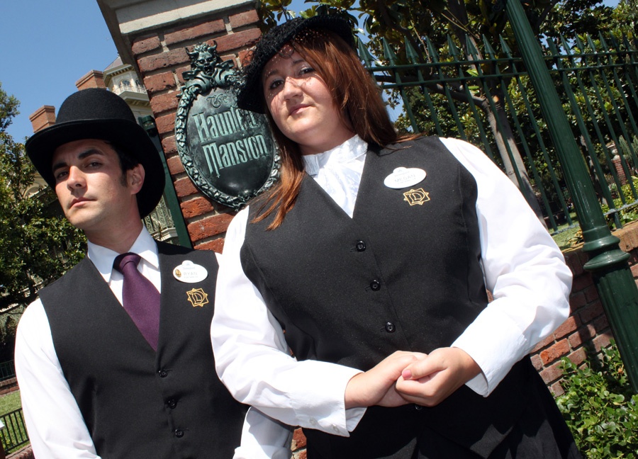 Two Haunted Mansion cast members stand in front of the entrance to the attraction