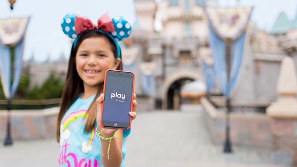 Little girl in front of Sleeping Beauty's castle holding up her phone