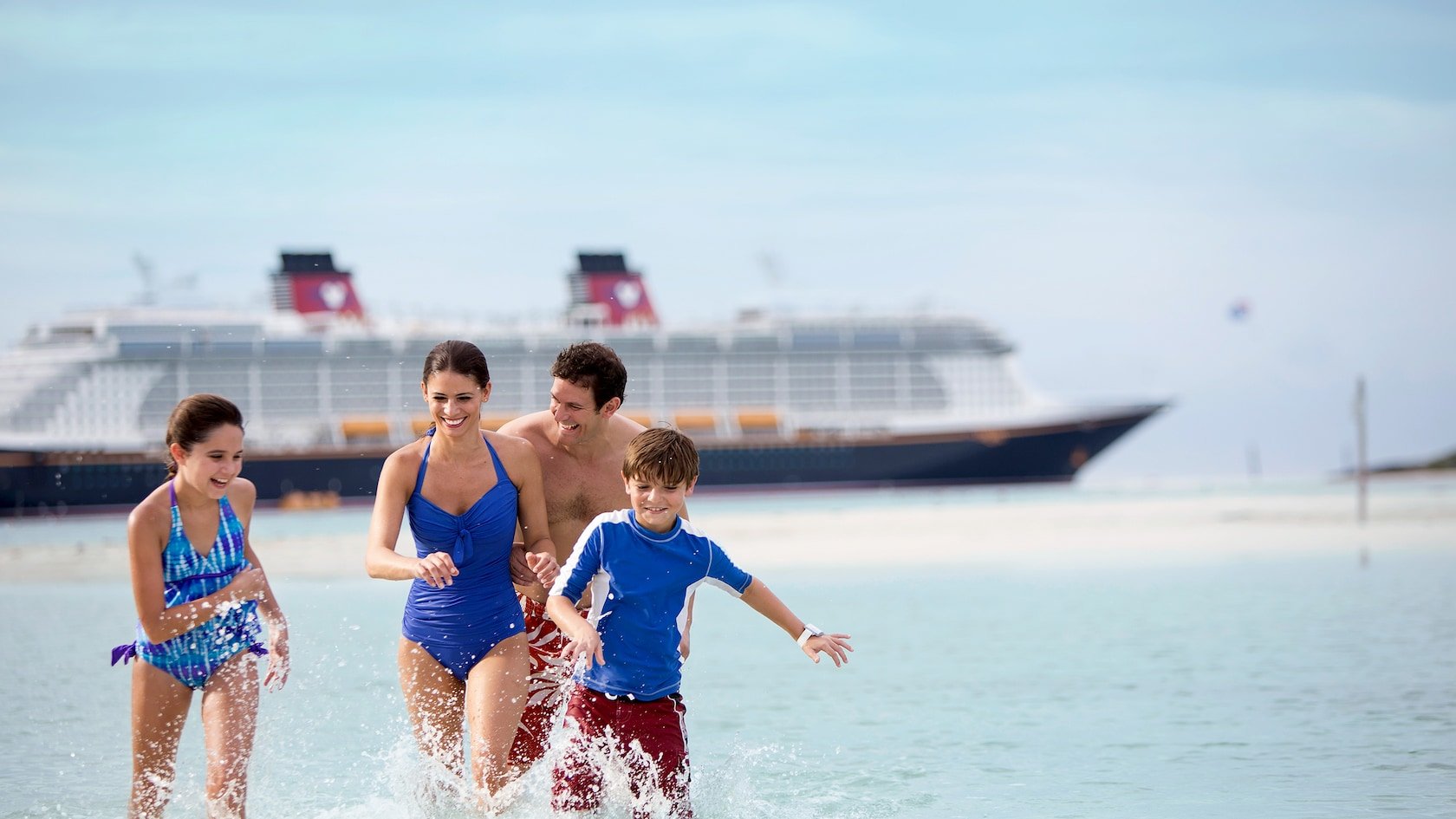 Family splashing in the ocean with Disney Cruise boat in the background