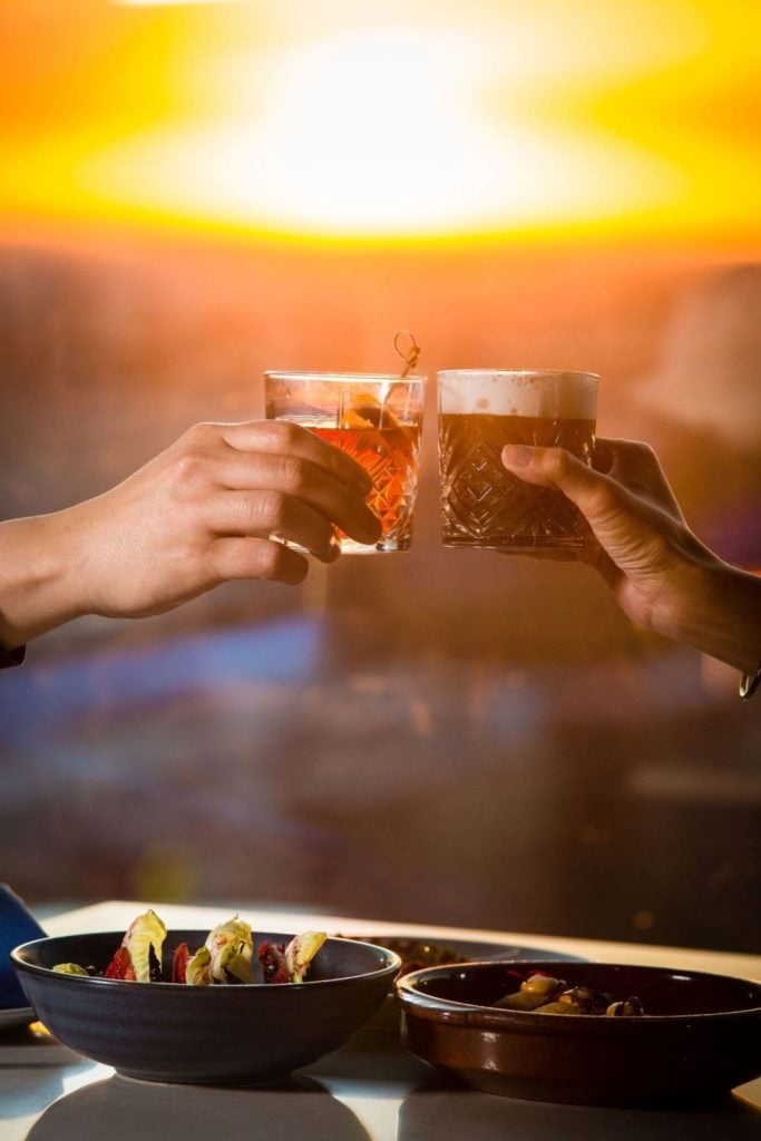 Two handcrafted cocktails clinking together at Top of the V rooftop restuarant