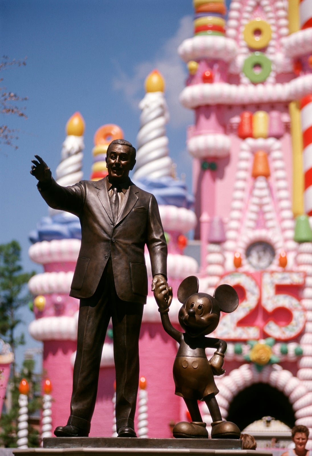 Statue of Walt Disney and Mickey Mouse in front of pink castle