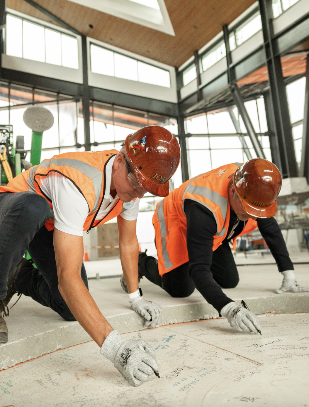 Men wearing hard hats and orange vests signing their names on concrete
